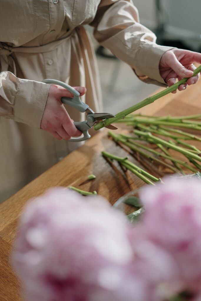 A florist carefully trims flower stems using pruning shears. Indoor setting.